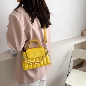 Detail of yellow crossbody bag with chain accessory worn over a pink blazer suit