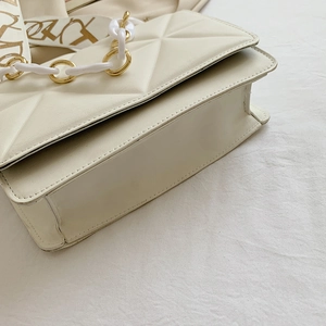 Detail of cream quilted crossbody bag featuring resin gold chain and patterned strap