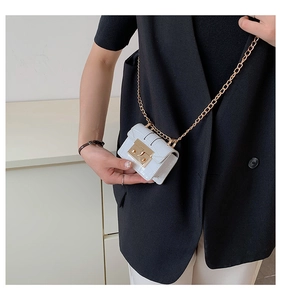 Détail du mini sac blanc motif crocodile avec fermoir doré et chaîne sur un blazer noir