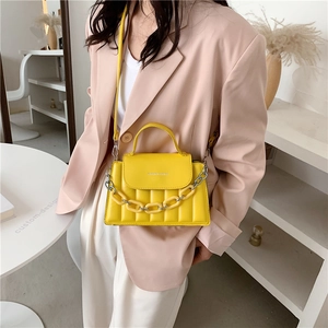 Close-up of a bright yellow quilted crossbody bag with metal chain and fashion text