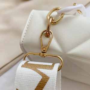 Detailed macro view of white quilted crossbody bag with gold hardware and wide strap