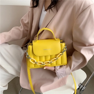 Close-up of bright yellow quilted crossbody bag with decorative thick chain and top handle