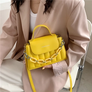 Detail of a bright yellow quilted shoulder bag featuring mixed resin and metal chain strap