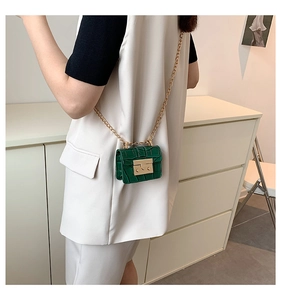 Close-up of deep green mini bag with crocodile texture and gold chain on white vest