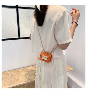 Detail of orange crocodile pattern mini bag with metal chain strap worn on the waist
