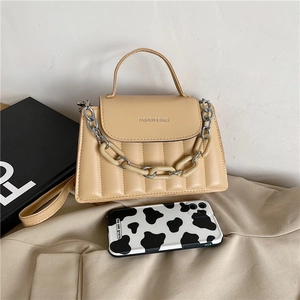 Detailed view of quilted beige handbag featuring silver chain strap and fashion text