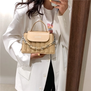 Detail of apricot quilted crossbody bag featuring chain strap and fashion text print
