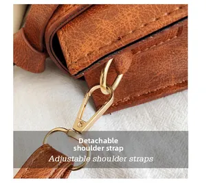 Détail de la ferrure dorée et de la bandoulière amovible en cuir sur un sac marron