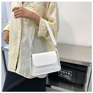 Modern white leather baguette bag worn over the shoulder by a model for size scale