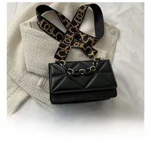 Macro shot of black quilted bag with gold chain and jacquard strap next to a mobile phone