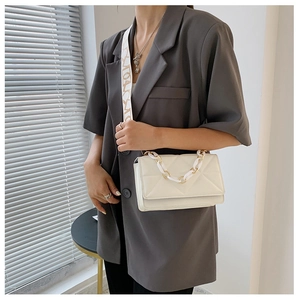 Detail of white quilted crossbody bag with chunky bicolor chain and patterned strap