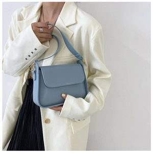 Detailed view of light blue square shoulder bag with gold hardware held by a model