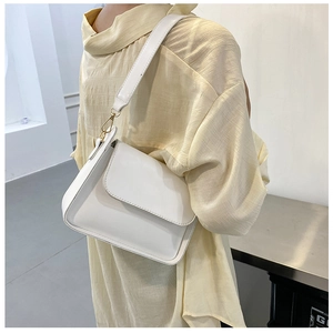 Detailed view of white crossbody bag with gold hardware on yellow textured shirt