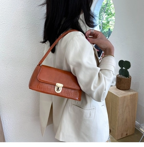 Detail of caramel crocodile pattern baguette bag with gold metal lock on a model