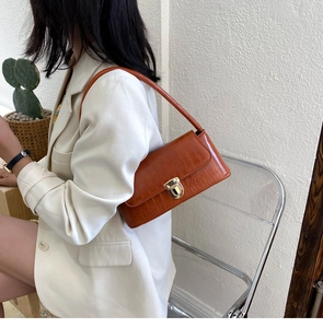 Brown crocodile embossed faux leather shoulder bag with gold clasp shown on a model