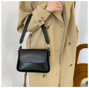 Detail of wide leather strap with gold buckle on a black minimalist baguette shoulder bag