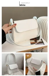 Detail view of white minimalist flap shoulder bag with gold metal hooks and wide strap