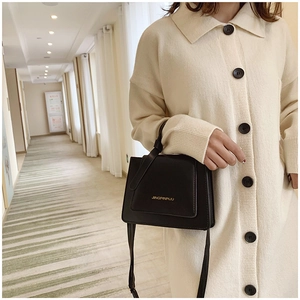 Détail d'un sac à rabat en cuir noir avec ferrures dorées et logo porté par un modèle