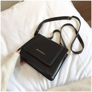 Gros plan d'un sac à bandoulière noir mat avec logo doré sur du lin blanc pur