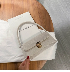 Close-up of beige crocodile pattern handbag with elegant gold clasp on wood table