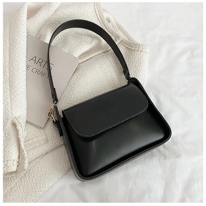Close-up of minimalist black leather crossbody bag on a textured white fabric background