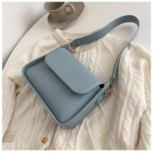 Detail of light blue flap crossbody bag with gold metal buckle on white knit fabric