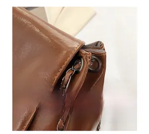 Close-up of brown leather tote bag showing dark gray metal rings and woven chain strap