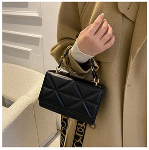 Detail of black geometric quilted handbag with gold chain handle and wide pattern strap
