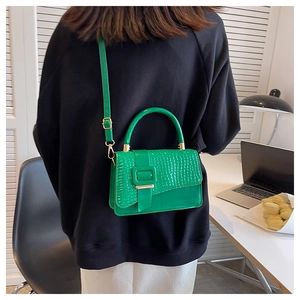 Detail der grünen Handtasche mit Krokodilprägung, Metallschnalle und verstellbarem Riemen