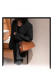 Détail d'un sac bandoulière en cuir brillant caramel avec chaîne porté par un mannequin