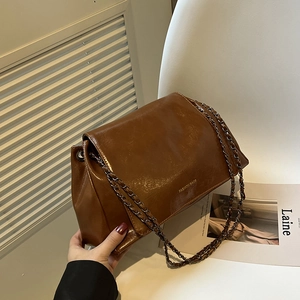 Gros plan sur un sac bandoulière en cuir ciré marron avec chaîne et texte imprimé