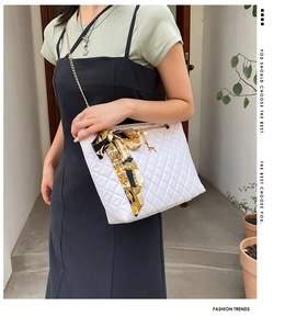 Close-up of white quilted shoulder bag with gold chain strap and silk scarf detail
