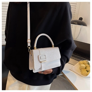 White faux crocodile leather handbag with metal buckle detail and top handle on a white desk