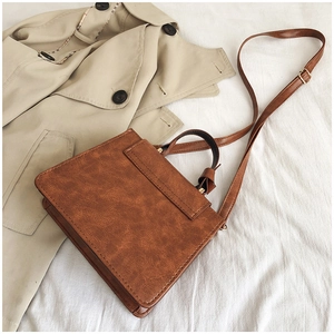 Gros plan d'un sac bandoulière vintage marron avec détails dorés sur un trench-coat beige