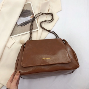 Détail du sac à bandoulière en cuir ciré marron foncé avec chaîne dorée et texte