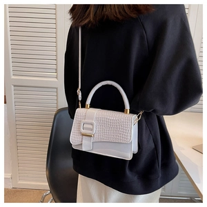 Detail of white crocodile pattern crossbody bag with golden buckle on a model