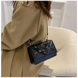 Elegant woman wearing a black quilted crossbody bag with a resin and gold chain strap