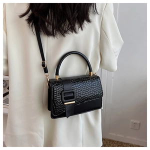 Details einer schwarzen Krokodil-Handtasche mit goldener Schnalle zu einem weißen Blazer
