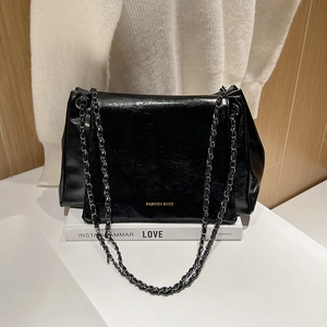 Chic black glossy leather crossbody bag with gold chain strap in a lifestyle setting