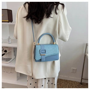 Close-up of light blue handbag featuring crocodile pattern flap and golden buckle detail