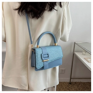 Detail of light blue faux crocodile leather bag with metal buckle and shoulder strap