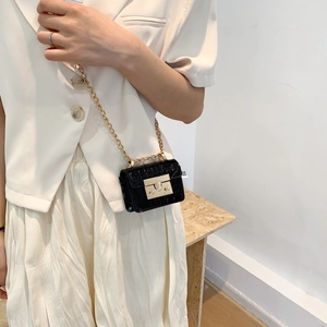 Mini black crocodile pattern square bag with gold chain strap worn by a female model