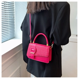 Detail view of the rose red crocodile embossed texture and square buckle on the handbag