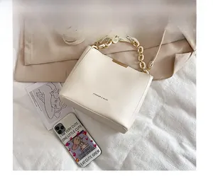 Close-up of beige leather bucket bag with decorative acrylic chain and fashion logo