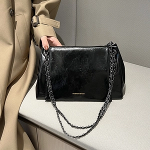 Détail du sac à bandoulière noir brillant avec chaîne argentée porté avec un trench