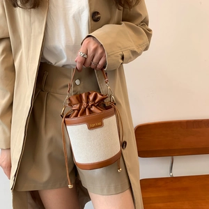 Dettaglio di una borsa a secchiello bicolore in tela indossata con un outfit kaki casual