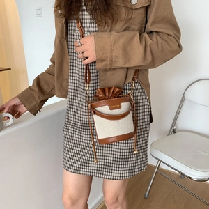 Dettaglio laterale di una borsa a secchiello in tela e pelle indossata da modella