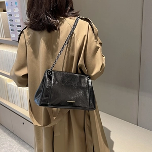 Sac cabas chic en cuir verni noir avec chaîne dorée porté sur un trench élégant