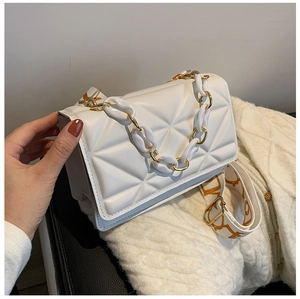 Close-up of white quilted leather crossbody bag with chic metal chain and wide woven strap
