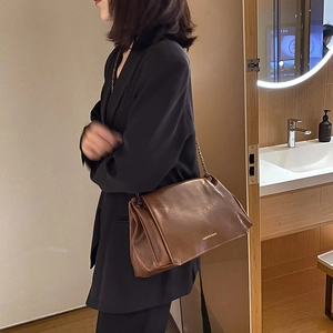 Vue latérale d'un sac bandoulière en cuir marron sur un mannequin en costume noir